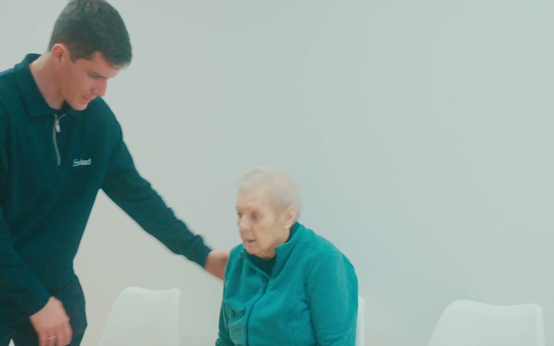 Fisioterapeuta ofreciendo la mano a una mujer mayor sentada para ayudarla a levantarse