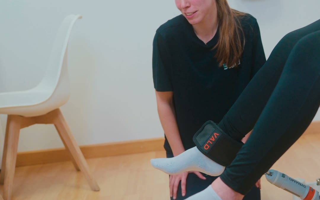 Fisioterapeuta colocando un medidor de fuerza en el tobillo de una paciente sentada