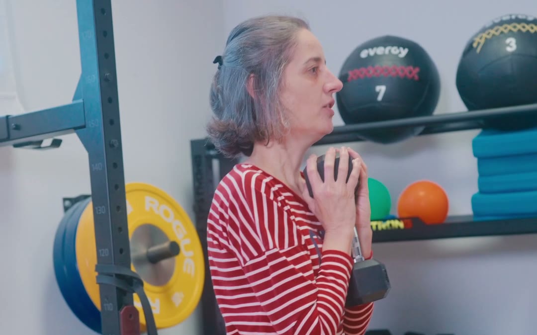Mujer sujetando un balón contra el pecho en la zona de fuerza, antes de una sentadilla